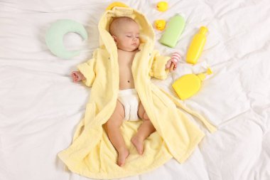Yataktaki banyo aksesuarları ve bornozlu tatlı bir bebek.