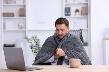 Klima. Ofiste battaniyeli bir adam soğuk hava yüzünden acı çekiyor.