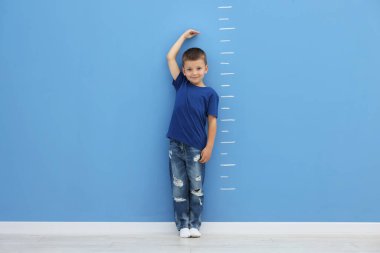 Mavi duvarın yanında boyunu ölçen küçük çocuk.