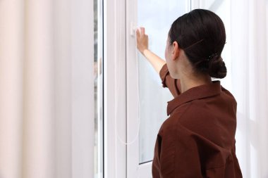 Genç bir kadın evinde modern bir pencere açıyor.