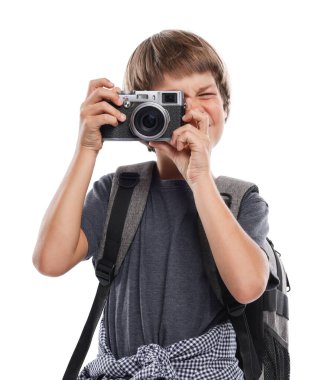 Meslek seçimi. Kameralı ve sırt çantalı küçük çocuk beyaz arka planda fotoğrafçı gibi davranıyor.