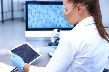 Genetik araştırması. Laboratuardaki masada tablet ve mikro plakalı bilim adamı çalışıyor.