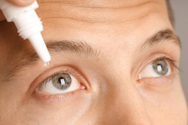 Gri arkaplanda göz damlası uygulayan adam, yakın plan