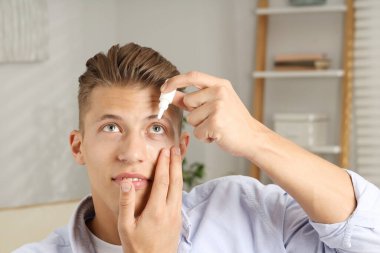 Evde göz damlası kullanan genç bir adam.