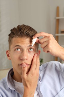 Evde göz damlası kullanan genç bir adam.