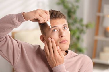 Evde göz damlası kullanan genç bir adam.