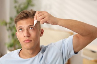 Evde göz damlası kullanan genç bir adam.