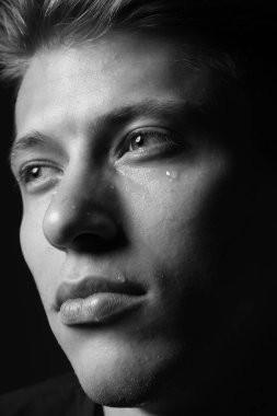 Üzgün adam karanlık arka planda ağlıyor, yakın planda. Siyah ve beyaz etkisi