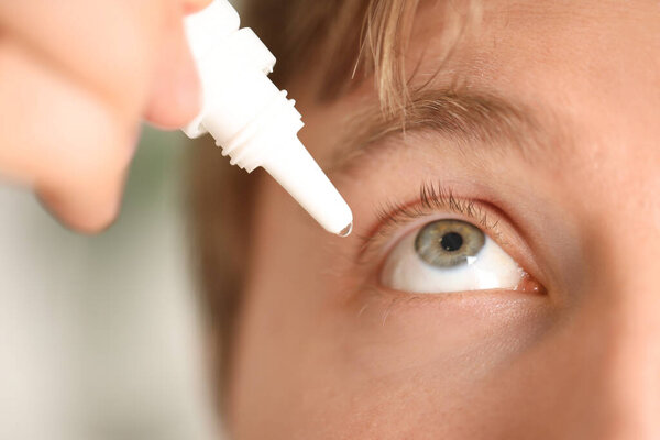 Man applying eye drops on light background, closeup