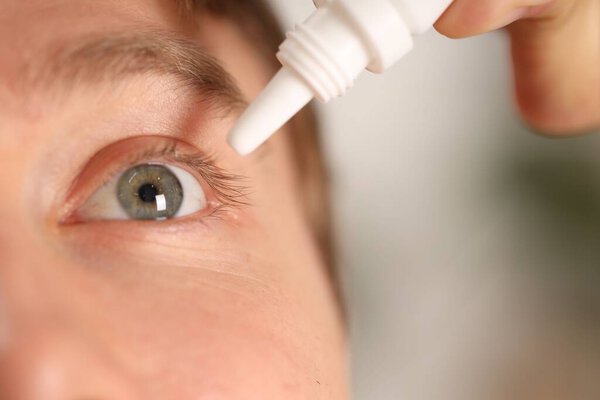 Man applying eye drops on blurred background, closeup. Space for text