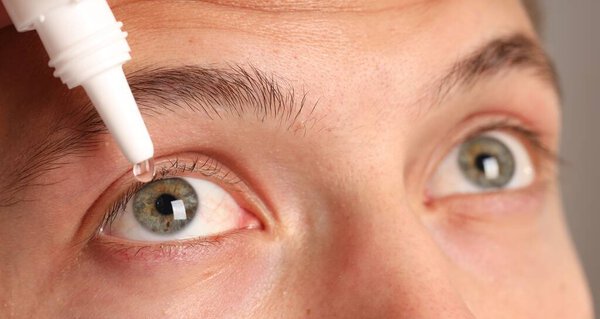 Man applying eye drops on grey background, closeup