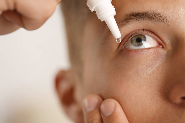 Man applying eye drops on light background, closeup