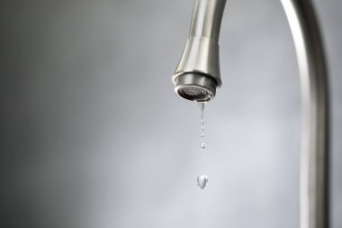 Su tasarrufu konsepti. Gri arka planda musluktan su damlıyor, yakın plan. Metin için boşluk