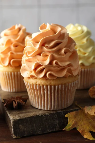 Renkli kremalı lezzetli kekler ve ahşap masada sonbahar dekoru, yakın plan.