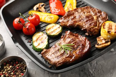 Izgara biftek, mantar, sebze ve baharatlı tava. Gri desenli masa, yakın plan.