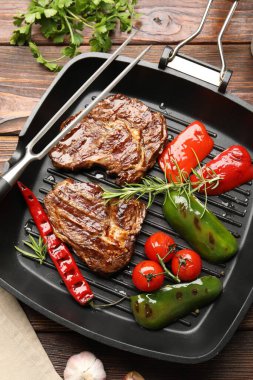 Izgara biftekli tava, biberiye, sebze ve ahşap masa üzerinde oyma çatal, düz uzanma