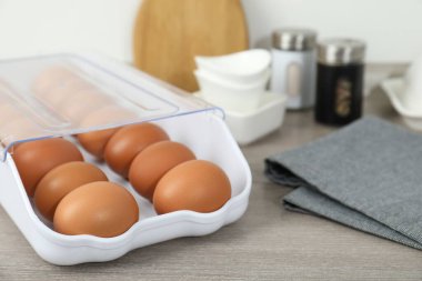 Plastik kabın içinde çiğ tavuk yumurtası ve ahşap tezgahın üzerinde mutfak aletleri, yakın plan.