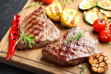 Bitki ve sebzeli leziz ızgara biftekler, koyu dokulu masa, yakın plan.