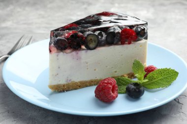 Piece of delicious cheesecake with berries and mint on grey table, closeup