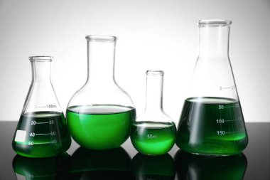 Masada beyaz arka plana karşı yeşil sıvı bulunan farklı bir laboratuar cam.