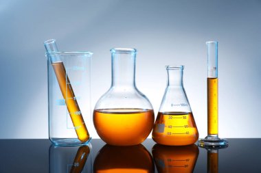 Ayna yüzeyinde gri arka planda turuncu sıvı bulunan farklı camlar.