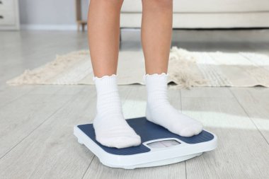 Küçük kız ağırlığını evde tartıyla ölçüyor, yakın plan.