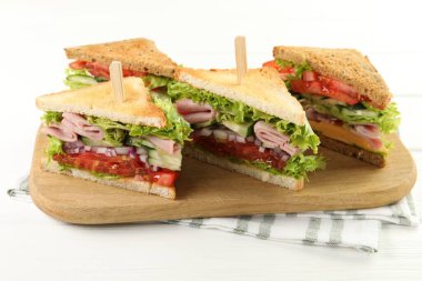 Tasty sandwiches with ham and vegetables on white wooden table, closeup