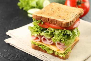Tasty sandwich with ham, cheese and vegetables on grey textured table, closeup