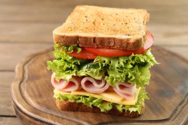 Tasty sandwich with ham, cheese and vegetables on wooden table, closeup