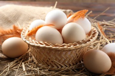 Hasır sepette çiğ tavuk yumurtası ve samandaki tüyler, yakın plan.