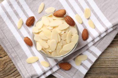 Fresh almond flakes and whole nuts in bowl on wooden table, top view