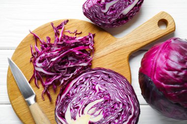 Whole and cut red cabbages, knife on white wooden table, flat lay
