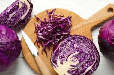 Whole and cut red cabbages, knife on white wooden table, flat lay