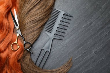 Beautiful hair strands in different colors and hairdresser's tools on grey background, flat lay. Space for text