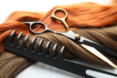 Farklı renklerde güzel saç telleri ve beyaz arka planda kuaför aletleri, yakın plan.