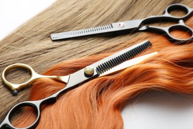 Farklı renklerde güzel saç telleri ve beyaz arka planda kuaför aletleri, yakın plan.