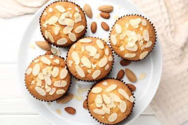 Tasty muffins with almond flakes and nuts on white wooden table, top view