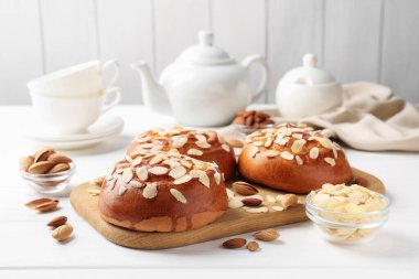 Tasty roll buns with almond flakes, nuts and tea set on white wooden table