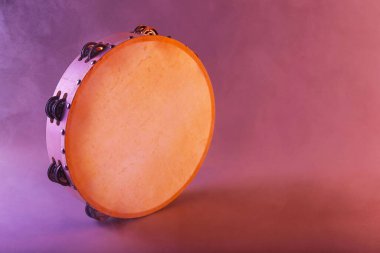 Tambourine in color light on pink background with smoke. Space for text