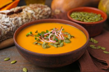 Delicious pumpkin soup with seeds and bread on wooden table, closeup