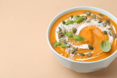 Delicious pumpkin soup with spices, cheese and sour cream in bowl on beige table, closeup. Space for text