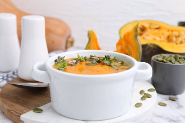 Delicious pumpkin soup with seeds and microgreens in bowl served on table, closeup