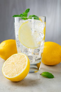 Limon meyveli ferahlatıcı su, açık gri masada buz ve nane, yakın plan.