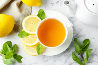 Aromatic tea in cup with lemons, mint and teapot on white marble table, flat lay