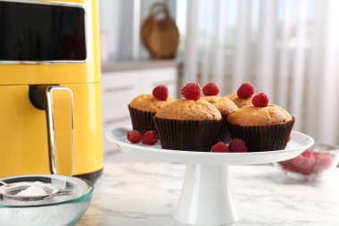 Mutfaktaki beyaz mermer masada ahududu ve hava kızartma makineli taze pişmiş muffinler.