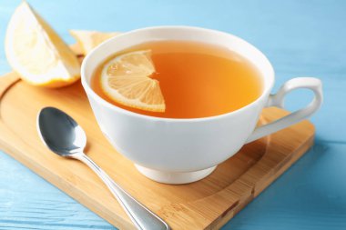 Aromatic tea in cup with lemon and spoon on light blue wooden table, closeup