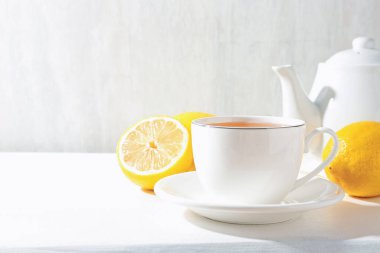Aromatic tea in cup, lemons and teapot on white table, closeup. Space for text