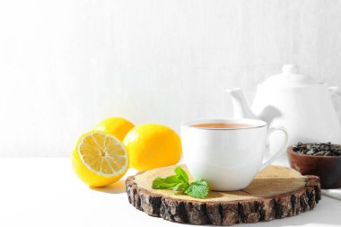 Aromatic tea in cup, lemons, mint, dry leaves and teapot on white table, closeup. Space for text