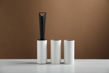 Lint roller and adhesive rolls on white marble table against brown background