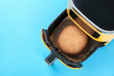 Air fryer with baked bread on light blue background, top view. Space for text